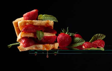 Belgian waffles with strawberries and honey on a black background. Copy space.の写真素材