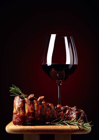 Grilled lamb ribs with rosemary and red wine on a wooden board. Copy space. Dark red background.の写真素材