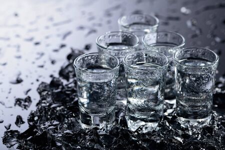 Damp glasses of vodka with ice on a black reflective background. Selective focus.の写真素材