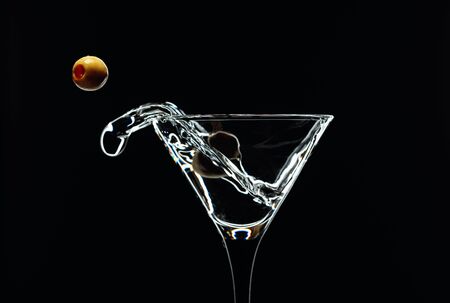 Martini splash. Silhouette of martini with green olives on a black background. の写真素材