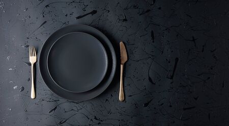 Empty black plate, fork and knife on a black background. Top view, copy space.の写真素材