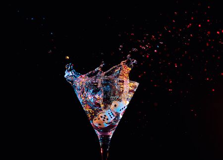 Dice fall in a glass of martini. Colourful cocktail in glass with splash on the dark background....