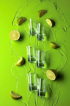Small shot glasses with lime slices and flowing tequila on a green background. Copy space.の写真素材