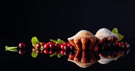 Muffins sprinkled with sugar powder on a black reflective background. Cranberry muffins with berries and mint. Copy space.の写真素材