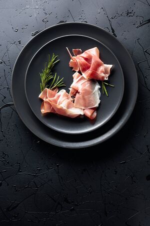Prosciutto and rosemary on a black plate. Top view, copy space.の写真素材