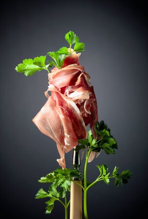 Thin sliced prosciutto with parsley on a fork. Traditional Italian cuisine. Black background.の写真素材