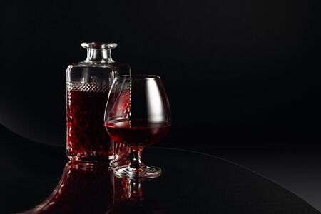 Glass of brandy and a carafe on a dark background. Fancy reflection on a black reflexive background....