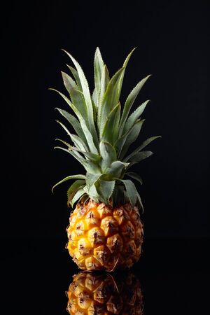 Ripe and juicy pineapple on a black reflective background.