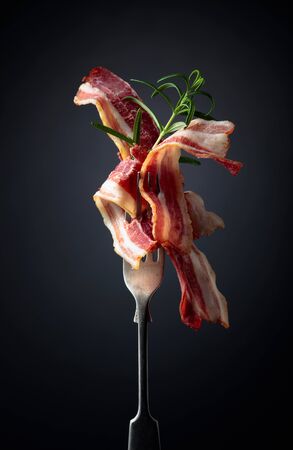 Slices of tasty fried bacon garnished with rosemary on a black background.の写真素材