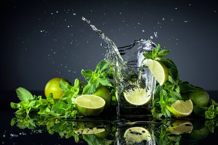 Cocktail with limes and mint on a black reflective background. Lime slice fall in glass with drink.の写真素材