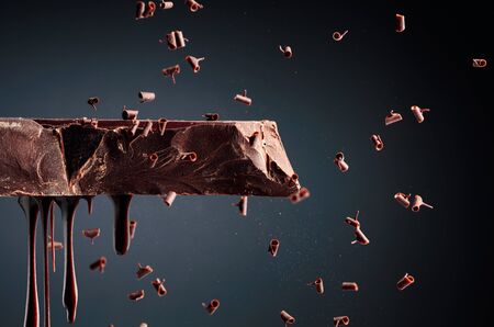 Melting piece of dark chocolate and falling chocolate crumbs on a black background.の写真素材