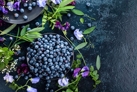Fresh juicy blueberries on a black plate. Summer still life with blueberries, colored sweet peas and meadow grasses. View from the top.の写真素材