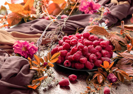 Fresh juicy raspberries on a black plate. Still life with, raspberries, flowers and meadow grasses.