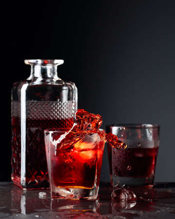 Pieces of ice fall into a frosted glass with whiskey. Alcoholic drink with natural ice on a black background. Copy space.の写真素材