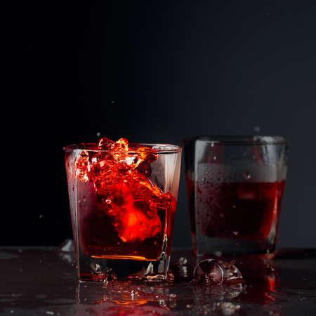 Pieces of ice fall into a frosted glass with whiskey. Alcoholic drink with natural ice on a black background. Copy space.の写真素材
