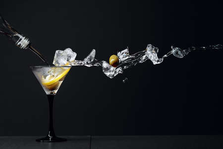 Martini with green olives, ice and lemon peel. Cocktail with splashes on a black background. Copy space.の写真素材