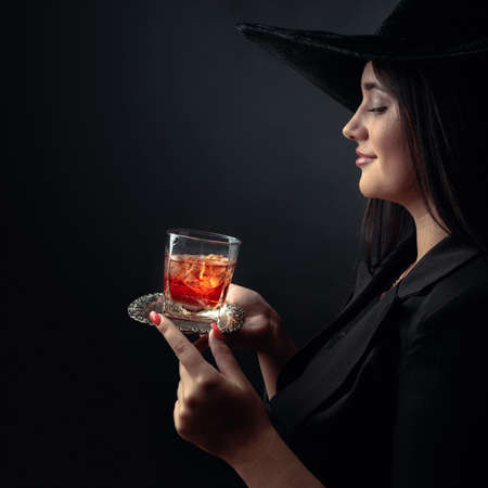 Attractive girl with alcoholic drink in frozen glass. Beautiful brunette in black hat holding glass...