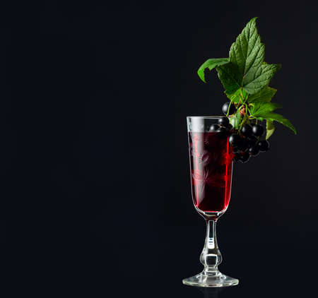 Glass of blackcurrant liqueur or syrup. Sweet drink and branch with leaves and ripe juicy berries on...
