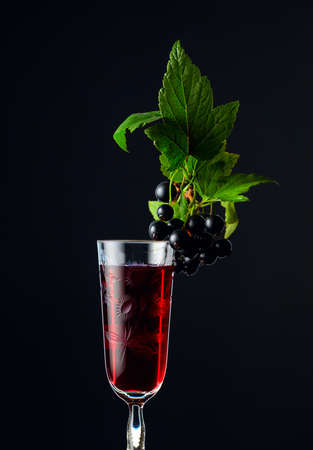 Glass of blackcurrant liqueur or syrup. Sweet drink and branch with leaves and ripe juicy berries on a dark background.の写真素材