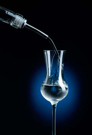 Vodka is poured from bottle into frozen glass with ice.
