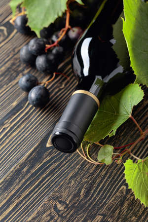 Unopened red wine bottle, vine twig, and ripe grapes on an old wooden table. Copy space.