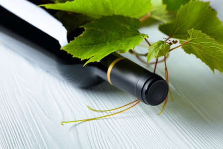 Unopened red wine bottle and vine twig on a white wooden table. Copy space.の写真素材
