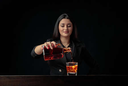 Attractive bartender girl pours an alcoholic drink into a glass with pieces of ice. Beautiful...