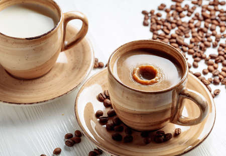Latte and coffee beans on a white wooden table. A drop of milk falls in a cup. Copy space.