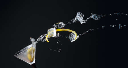 Martini with green olives, ice and lemon peel. Cocktail with splashes on a black background. Copy space.の写真素材