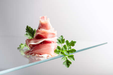 Prosciutto with parsley on a glass table, copy space.の写真素材