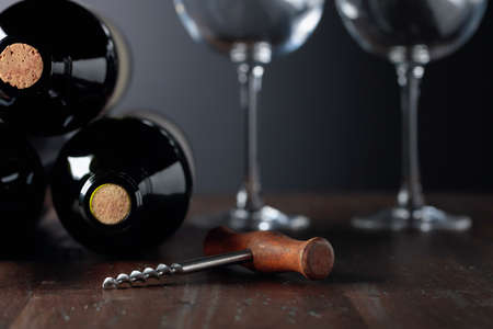 Unopened bottles of red wine, corkscrew, and empty wine glasses on an old wooden table. Copy space.