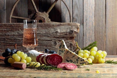 Rustic still life with wine and snacks. On an old wooden table wine, blue cheese, dry-cured sausage, grapes, and rosemary. Simple and tasty food.の写真素材