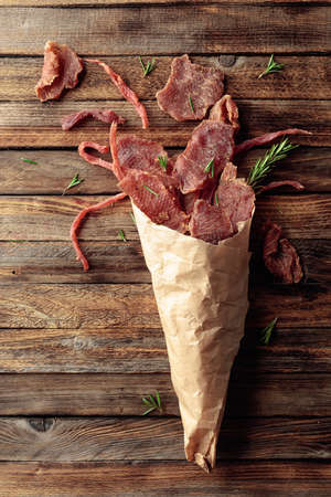 Slices of spicy dry-cured meat with rosemary in a paper bag on an old wooden table. Top view. Copy space.の写真素材