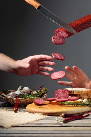 Sandwich with salami on a cutting board. Sliced sausage with rosemary, red pepper, and garlic on an old wooden table.の写真素材