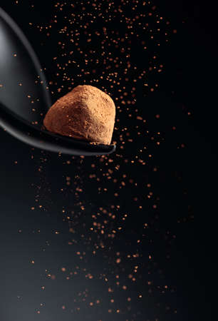 Chocolate candy truffle and flying cocoa powder on a dark background. Copy space.