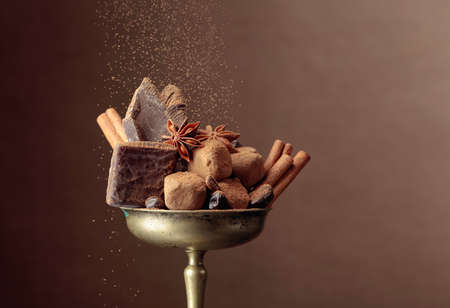Various chocolates with ingredients.  In an old brass bowl candy, coffee beans, cinnamon, anise, and pieces of broken black chocolate. Copy space.の写真素材