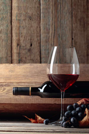 Red wine and a bunch of grapes on an old wooden table in the wine cellar. Selective focus.