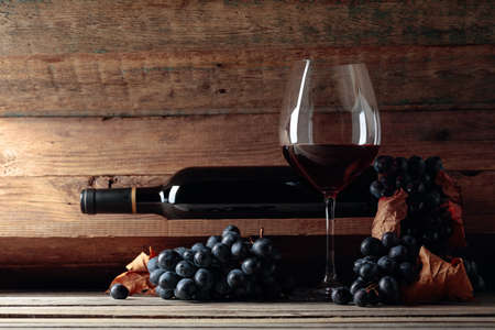 Red wine and a bunch of grapes on an old wooden table in the wine cellar. Selective focus.の写真素材