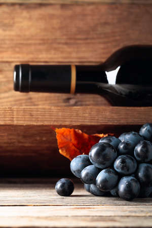 Bottle of red wine and a bunch of grapes on an old wooden table in the wine cellar. Selective focus.の写真素材