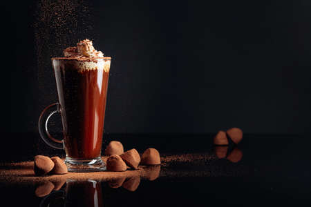 Truffles and glass of hot chocolate with whipped cream. Sweets and drink on a black reflective...