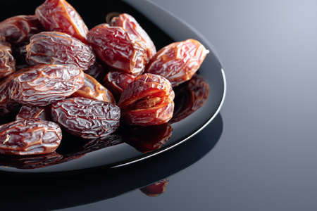 Dried sweet dates on a black plate, black reflective background.