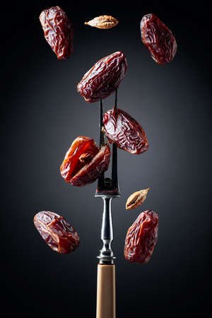 Dried sweet dates on a fork, black background.