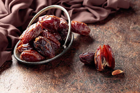 Dried sweet dates in a metal dish on an old brown table.