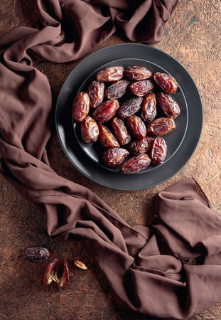 Dried sweet dates on a black plate, top view.