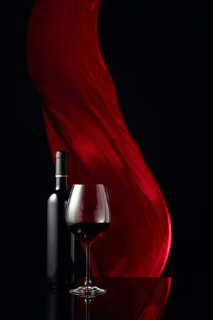 Ðottle and glass of red wine on a black reflective background. Red cloth flutters in the background. Copy space.の写真素材