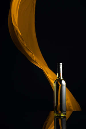 Ðottle of white wine on a black reflective background. Yellow cloth flutters in the background. Copy space.の写真素材