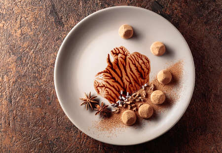 Chocolate truffles on a beige plate with chocolate sauce. Sweets are sprinkled with cocoa powder,...