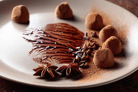 Chocolate truffles on a beige plate with chocolate sauce. Sweets are sprinkled with cocoa powder,...