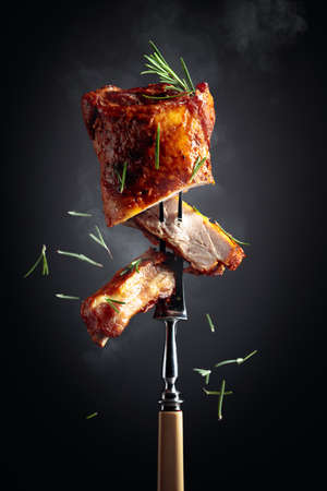 Grilled pork ribs on a fork. Grilled meat sprinkled with rosemary on a black background.の写真素材