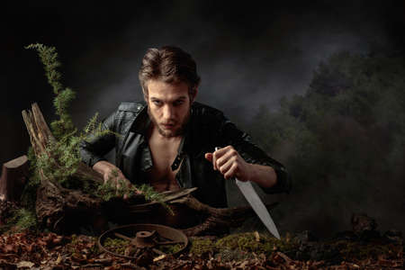 Portrait of a young man with a knife. A serious man in a black leather jacket with a knife looks menacingly at the camera. Copy space.の写真素材